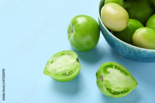 Bowl with fresh green tomatoes on blue background, closeup