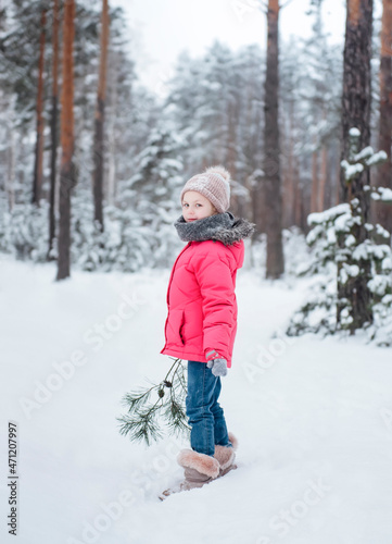 Little girl in a bright jacket plays in the winter forest