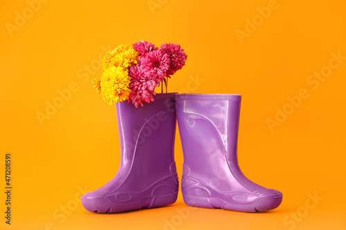 Rubber boots and flowers on color background