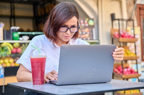 Middle-aged woman with a laptop at a table in an outdoor sidewalk cafe with fresh juice © Valerii Honcharuk