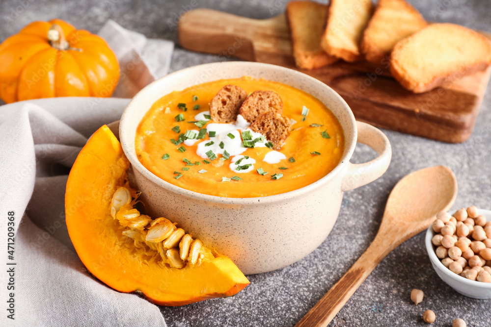Pot with delicious pumpkin cream soup on grey background Pot with delicious pumpkin cream soup on grey background