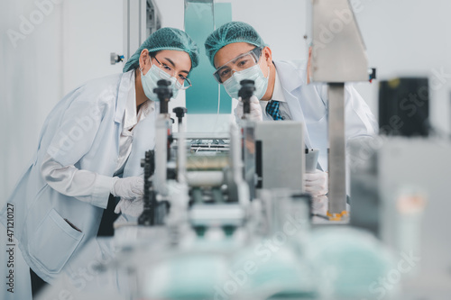 Both male and female Asian scientists are outfitted with protective gear. Examining the factory's machinery and materials used in the mask-making process. Covid 19 is a piece of preventive equipment.