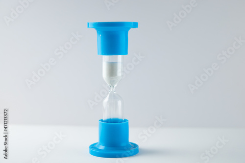 hourglass blue with white sand on a gray and white background 