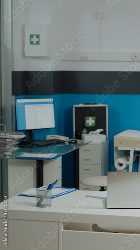 Nobody in doctors office with modern funiture at medical facility. Empty examination cabinet for healthcare specialist. Close up of white desk with laptop, stethoscope and pens