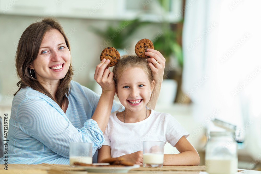 happy loving family, mom and daughter, playing sitting at table and having breakfast at home in morning. woman and girl eat oatmeal cookies and drink cow's milk, and have nice time together in kitchen happy loving family, mom and daughter, playing sitting at table and having breakfast at home in morning. woman and girl eat oatmeal cookies and drink cow's milk, and have nice time together in kitchen