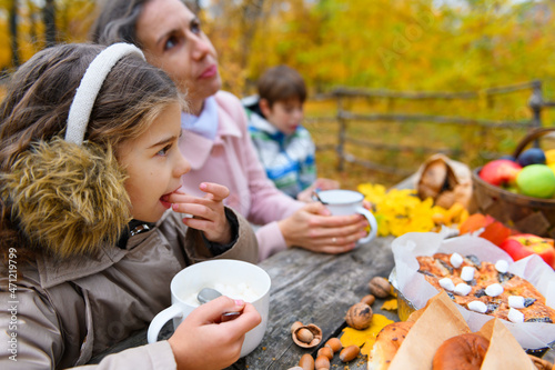 Portrait of a happy family in an autumn park. People are sitting at the table, eating and talking. Posing against the background of beautiful yellow trees. They are happy together.