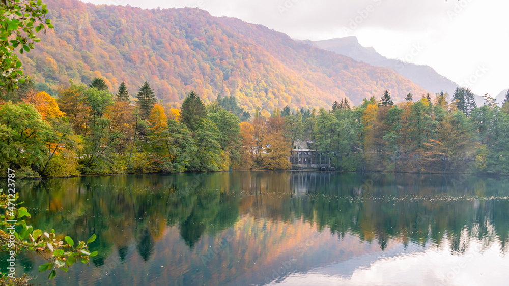 Karst blue lake high in the mountains. The depth of the karst lake Cerik-Kel is 279 meters. View of the mountain lake and mountains in autumn. Fallen leaves from trees float in the lake. Karst blue lake high in the mountains. The depth of the karst lake Cerik-Kel is 279 meters. View of the mountain lake and mountains in autumn. Fallen leaves from trees float in the lake.