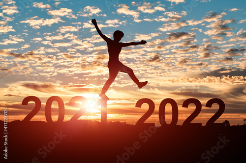 Concept of new year 2022. Silhouette of man jumping from 2021 to 2022 with cloud sky sunset background.