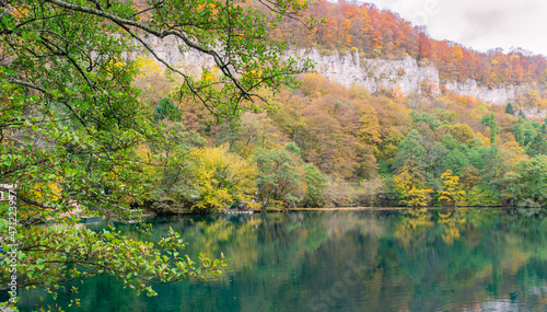 Karst blue lake high in the mountains. The depth of the karst lake Cerik-Kel is 279 meters. View of the mountain lake and mountains in autumn. Fallen leaves from trees float in the lake.