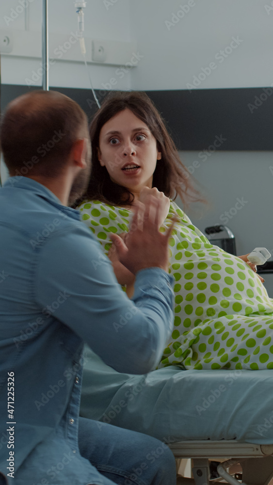 Obraz premium Caucasian pregnant woman getting labor contractions sitting in hospital ward. Young person preparing for painful child delivery at maternity clinic holding hands with nervous husband