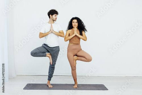a woman and a man practice a paired yoga asana in a white room