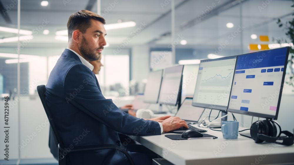 Young Businessman Using Computer in Modern Office with Colleagues. Stylish Handsome Manager Working on Desktop Computer Analyze Business Projects, Finance Data. Employees Work in Open Office. Young Businessman Using Computer in Modern Office with Colleagues. Stylish Handsome Manager Working on Desktop Computer Analyze Business Projects, Finance Data. Employees Work in Open Office.