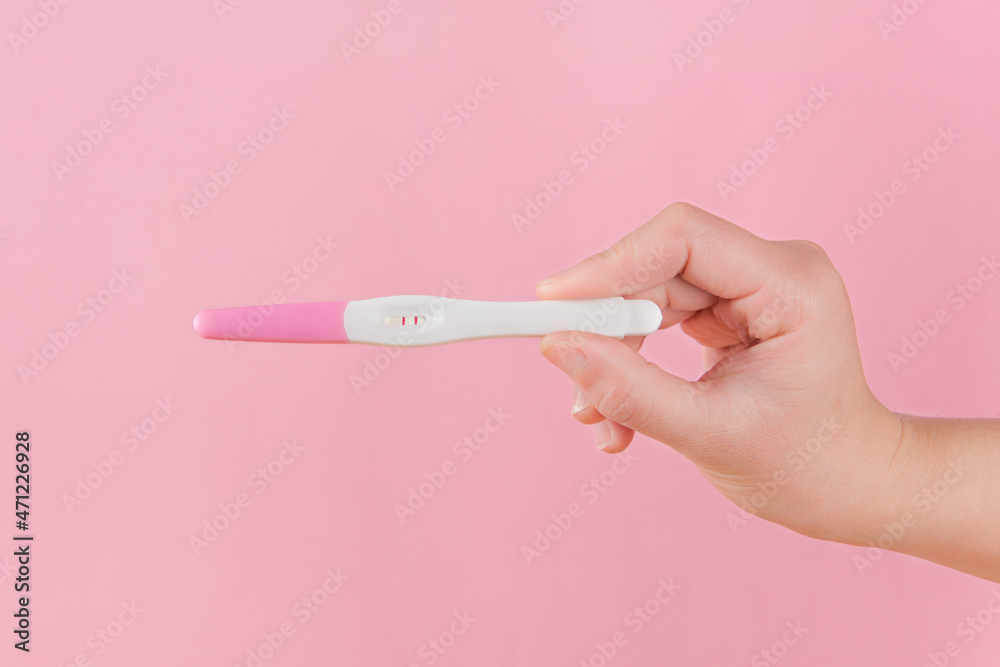 Woman is holding positive pregnancy test on pink background - obrazy, fototapety, plakaty 
