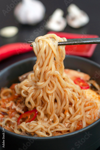 chinese chopsticks hold noodles. Ramen is a popular dish of traditional Korean cuisine. Asian soup with noodles, chicken breast, egg, mushrooms, broth, hot sauce and spices. Vertical shot, close-up.