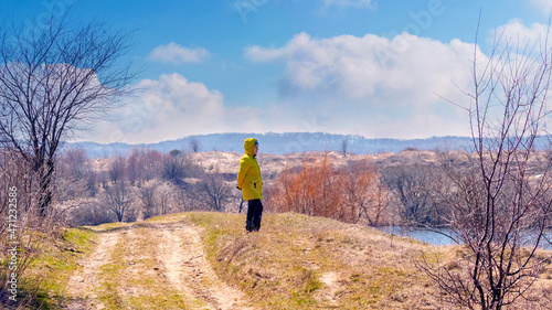 Woman in a warm jacket by the river during a walk in early spring