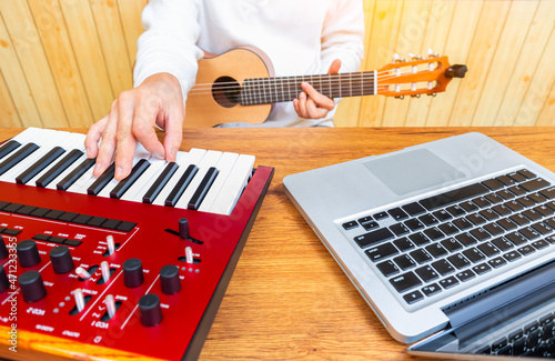 male songwriter playing keyboard and acoustic guitar for creating a hit song on laptop computer. songwriting concept