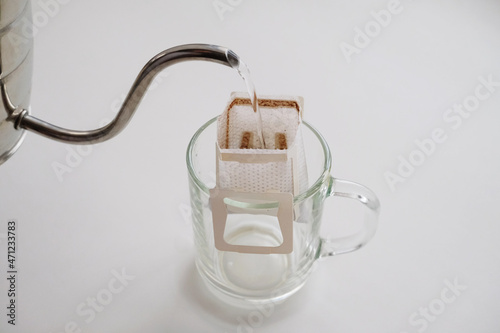 Drip bag coffee on glass cup. Pouring water from gooseneck kettle. Instant freshly brewing method