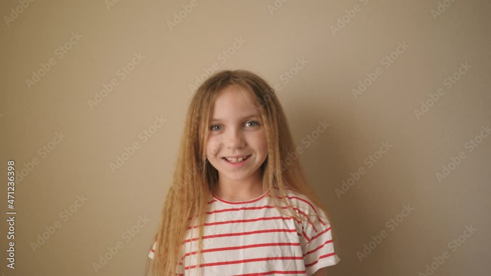 Little smiling girl with blonde hair looking into camera indoor. Close up emotions of beautiful kid with glad expression on her face. Portrait of happy female child against the background of wall Little smiling girl with blonde hair looking into camera indoor. Close up emotions of beautiful kid with glad expression on her face. Portrait of happy female child against the background of wall