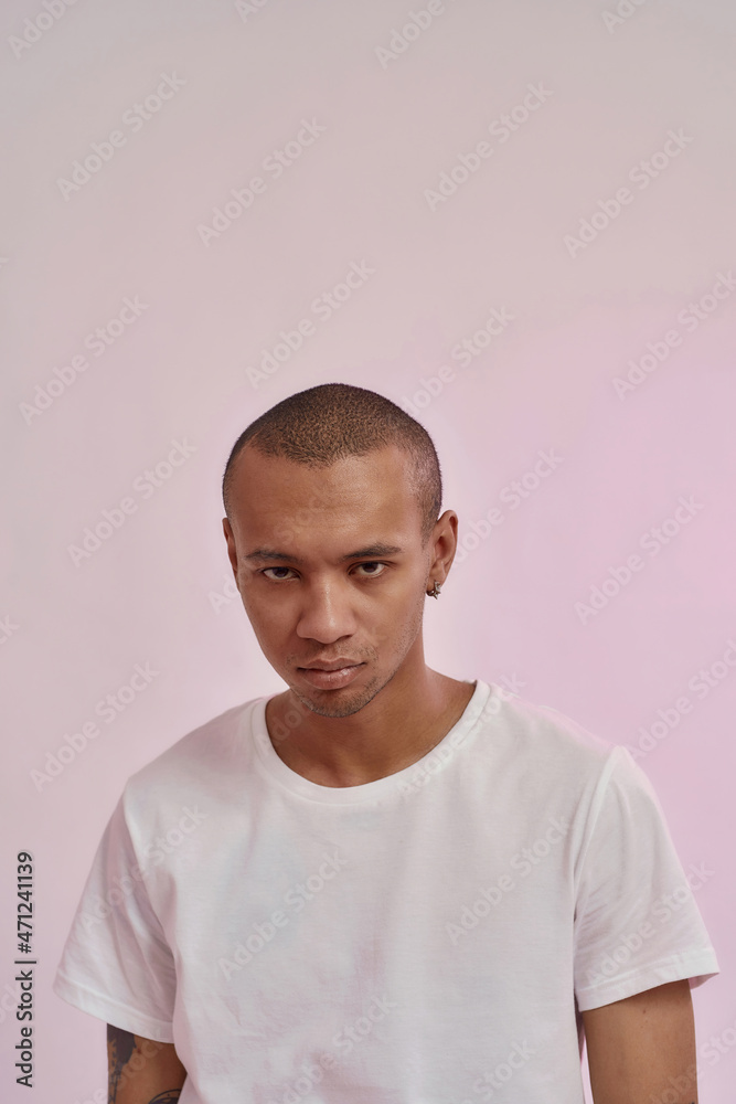 Portrait of serious young mixed race man in casual white t shirt looking at camera, standing isolated over pink background Portrait of serious young mixed race man in casual white t shirt looking at camera, standing isolated over pink background