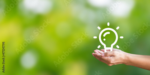 Hand holding light bulb icon on green background. Demonstrates energy savings and turns to solar and natural energy. Saving energy is helping both ourselves and the planet.