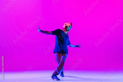 Young man, break dancing dancer headed of dog's head dancing isolated over bright magenta background at dance hall in neon light.