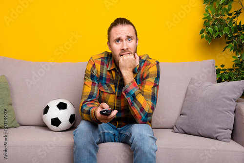 Photo of nervous football fan guy sit sofa watch intense match translation wear plaid shirt isolated yellow color background