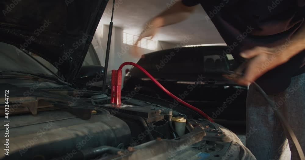 Young man attaching positive and negative cables for start engine of