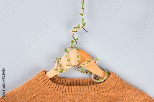 Orange sweater on hangers entwined with plants on gray background with copyspace. Conscious and environmentally friendly consupmtion - new modern trends in shopping. Zero waste. Slow fashion concept.