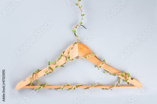 Hangers entwined with plants on gray background with copyspace. Conscious and environmentally friendly consupmtion - new modern trends in shopping. Zero waste. Slow fashion concept.