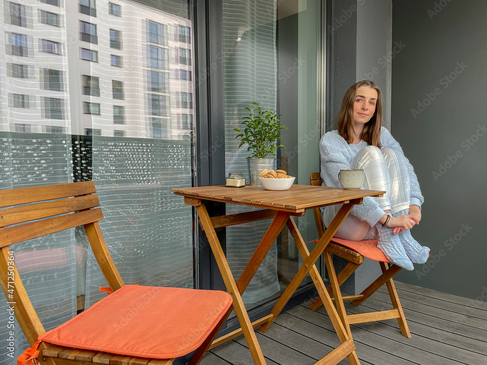 Pretty girl in pajama having breakfast and sitting with her arms around her knees on balcony or terrace in the morning in city. Pretty girl in pajama having breakfast and sitting with her arms around her knees on balcony or terrace in the morning in city.