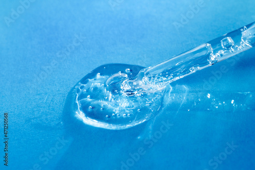 Facial serum or essential oil in glass pipette with bubbles pouring on blue background. Cosmetic product drop with vitamin C and hyaluronic acid closeup. Beauty skin treatment research. © gorina_anna