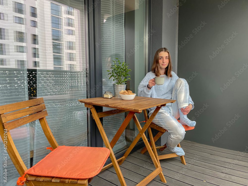 Pretty girl in pajama holding a cup of coffee in her hand on balcony or terrace in the morning in city.