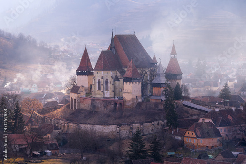 Gorgeous view of the castle church. The architectural structure of the Middle Ages. Fortification in brown tones. Smoke enveloped the castle. Sunny day. Saxon Village. Romania. Biertan. Transylvania.  photo