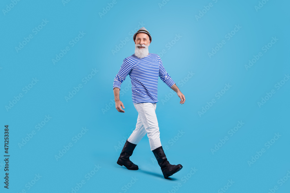 Full length photo of happy positive old man walk empty space good mood smile isolated on blue color background Full length photo of happy positive old man walk empty space good mood smile isolated on blue color background