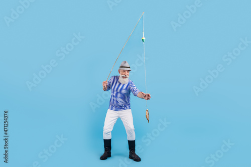 Full body photo of happy positive old man catch fish rod smile good mood isolated on blue color background