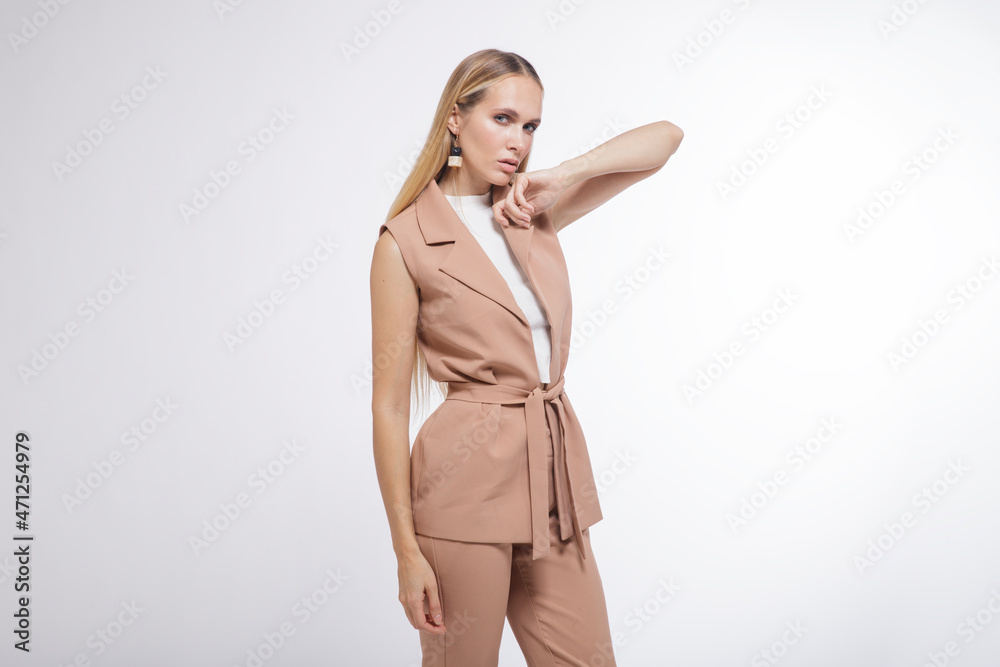 High fashion photo of a beautiful elegant young woman in a pretty beige suit, pants, trousers, vest, boots posing over white, soft gray background. Studio Shot, portrait. Blonde High fashion photo of a beautiful elegant young woman in a pretty beige suit, pants, trousers, vest, boots posing over white, soft gray background. Studio Shot, portrait. Blonde