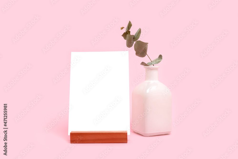 Eucalyptus branch in vase and paper card mockup in front of pink pastel background. Simplicity composition with copyspace. Eucalyptus branch in vase and paper card mockup in front of pink pastel background. Simplicity composition with copyspace.