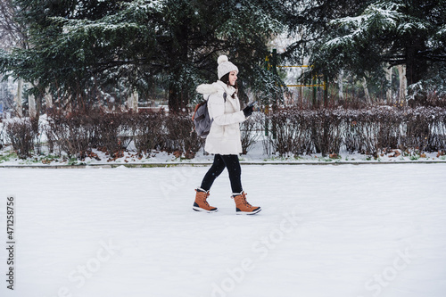 caucasian young woman walking outdoors in city during winter while snowing, using mobile phone.winter lifestyle