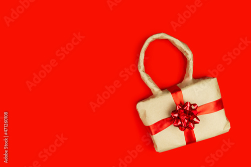 Eco rustic beige recycled Christmas new year gift, bag wrapped in craft paper with red ribbon on red color background. Holiday present. Care package. Vintage parcel. Festive congratulation.