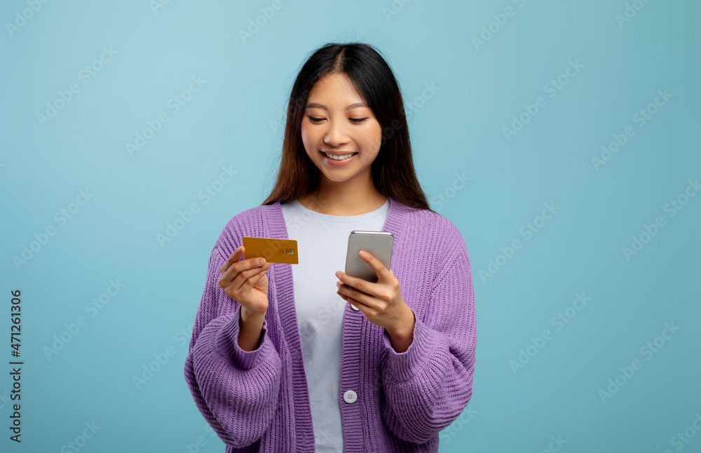 Online payments. Asian lady using smartphone and credit card, transferring money or paying bills, blue background Online payments. Asian lady using smartphone and credit card, transferring money or paying bills, blue background