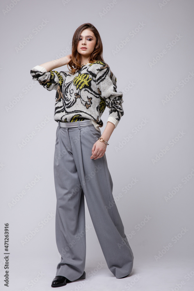 Fashion photo of a beautiful elegant young woman in a pretty gray pants, trousers, blouse, bicolor accessories, boots posing over white, soft gray background. Brown hair. Studio Shot. Fashion photo of a beautiful elegant young woman in a pretty gray pants, trousers, blouse, bicolor accessories, boots posing over white, soft gray background. Brown hair. Studio Shot.
