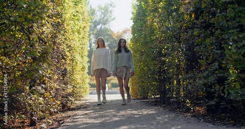 Young women does defile in slow motion the park. Fashion stylish video of two girls in short skirts walking to the camera outdoors, 4k 60p Prores HQ photo