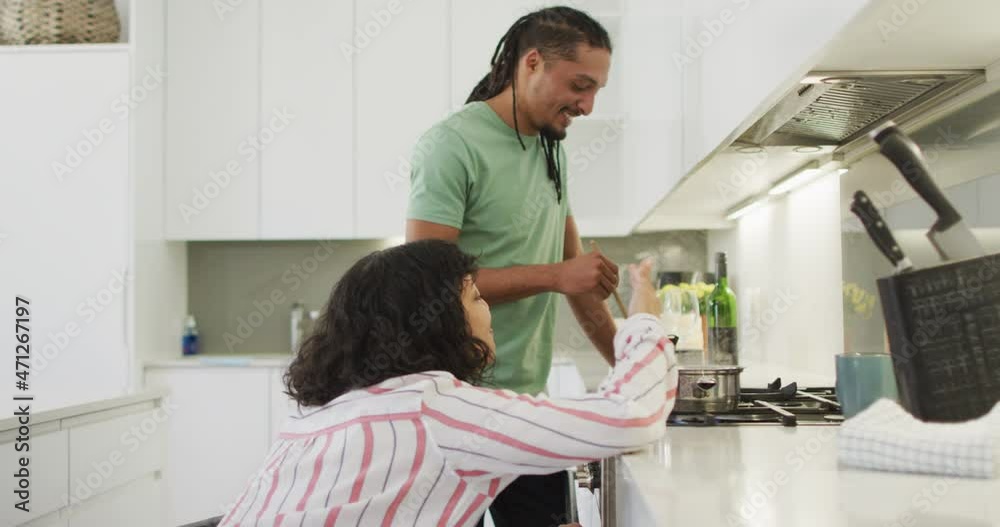 Happy biracial woman in wheelchair talking with smiling male partner preparing food in kitchen