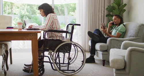 Wallpaper Mural Happy biracial woman in wheelchair using laptop, with male partner talking on phone in living room Torontodigital.ca