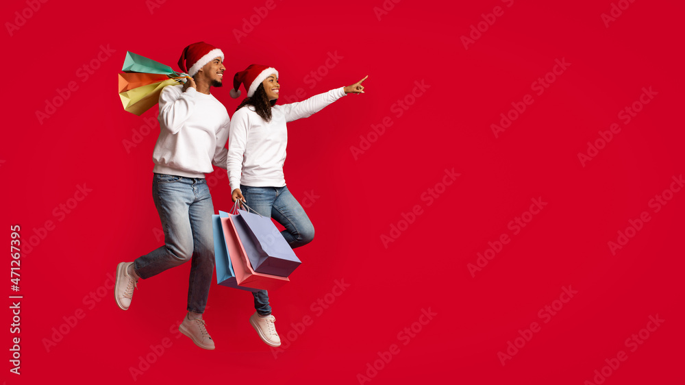 Emotional african american lovers in Santa hats holding shopping bags Emotional african american lovers in Santa hats holding shopping bags