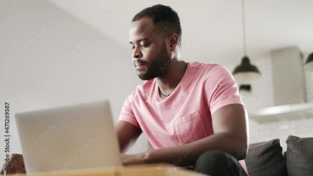 African positive man typing something by laptop and writing in notepad at home on the sofa African positive man typing something by laptop and writing in notepad at home on the sofa