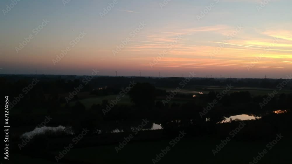 Aerial pan view of vast meadows with windmills and river cross by under a colorful sunset. Belgium Aerial pan view of vast meadows with windmills and river cross by under a colorful sunset. Belgium
