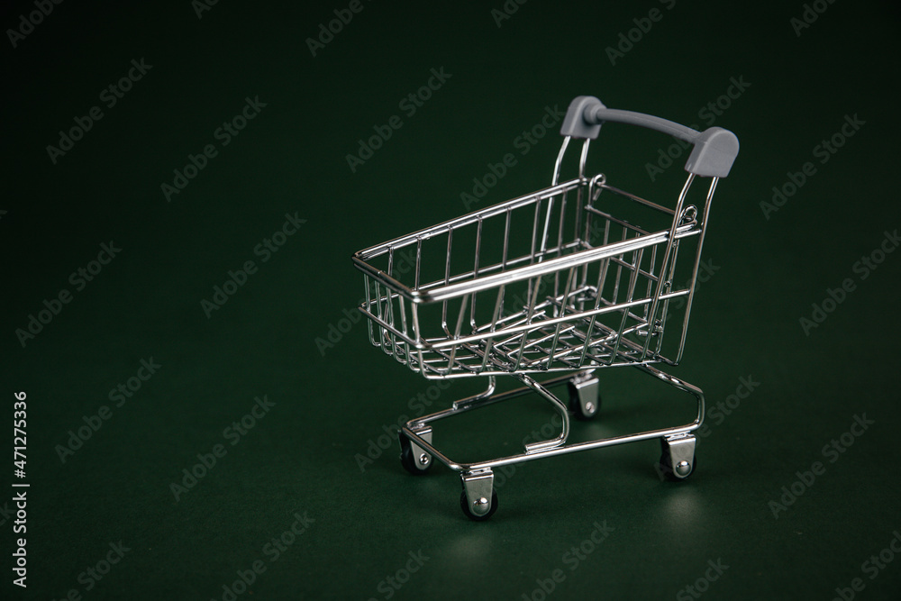 Empty shopping cart, shopping trolley with gift box on green background. 