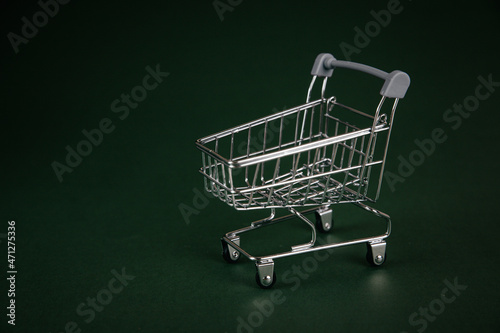 Empty shopping cart, shopping trolley with gift box on green background. 