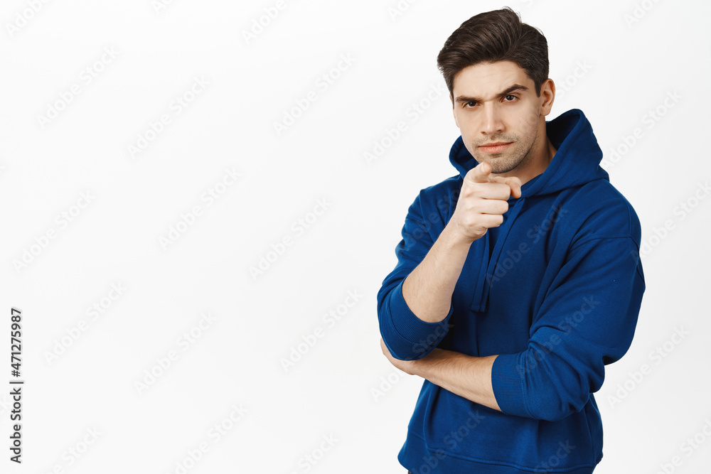 Suspicious man with frowned face, pointing finger at camera and looks serious at camera, stands over white background Suspicious man with frowned face, pointing finger at camera and looks serious at camera, stands over white background